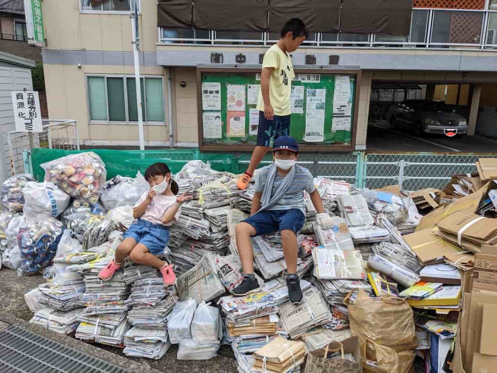 廃品回収終了後の写真。資源ごみが山になっている上に子ども会の子ども達が乗って写っている。